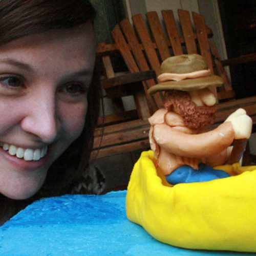 woman smiling looking at cake with a fondant canoe and paddling man cake topper