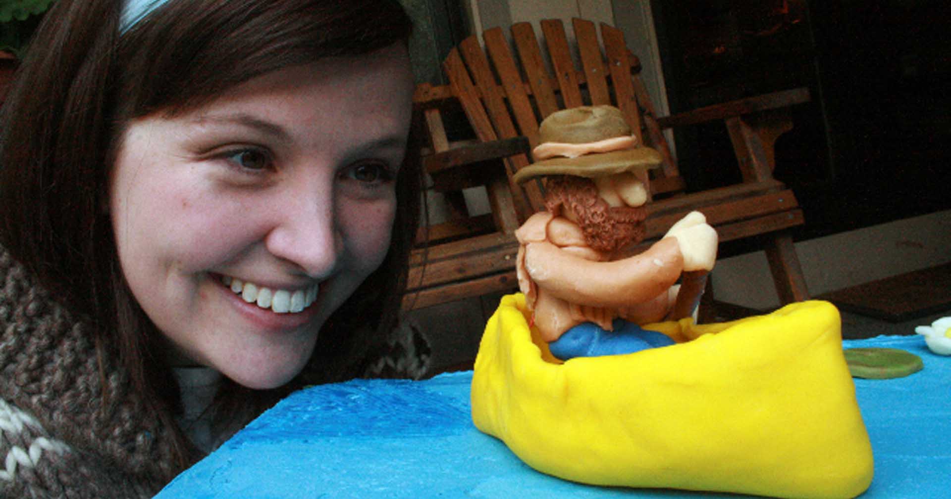woman smiling looking at cake with a fondant canoe and paddling man cake topper