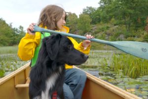 young girl paddling a canoe with her dog