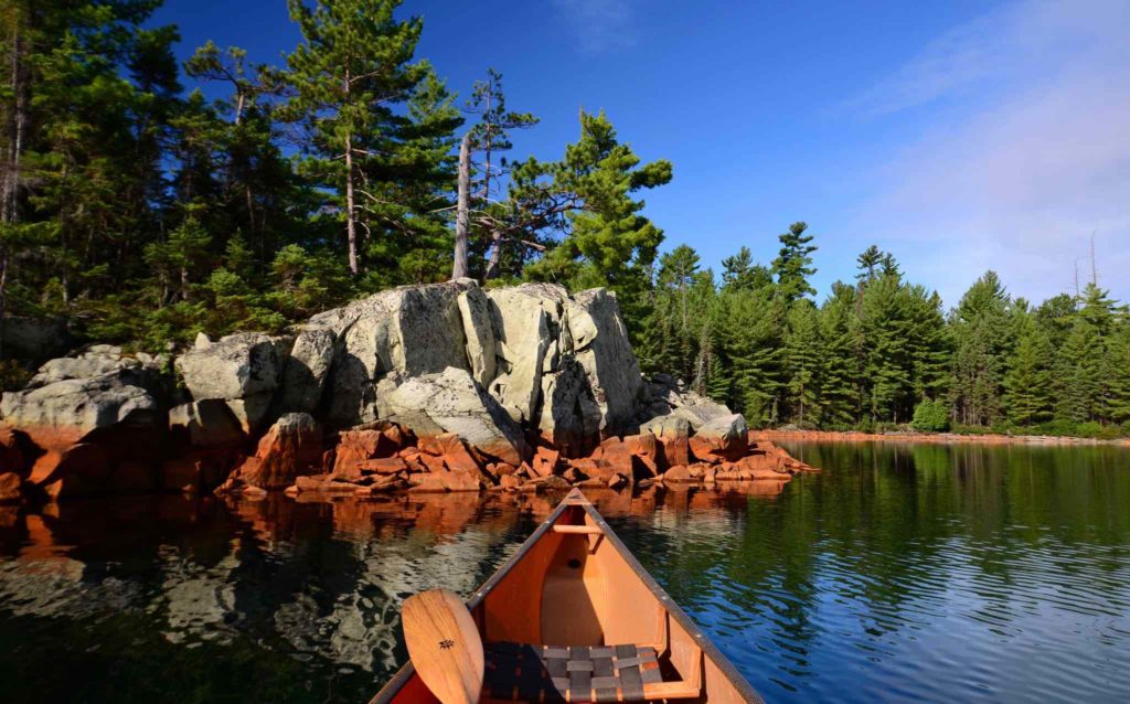 Lake Chiniguchi shoreline featuring the bow of a canoe and a Badger canoe paddle. Photo Credit: Chris Mayne