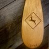 Detailed view of a Cherry La Bonga canoe paddle blade with laser engraved deer crossing sign motif on a barn board background