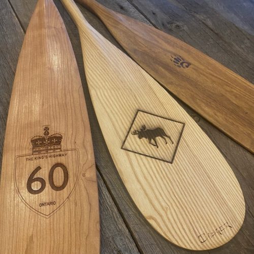 Depicting detail view of various Badger canoe paddles with a Hwy 60 Laser Engraving and a Moose Crossing Sign Motif