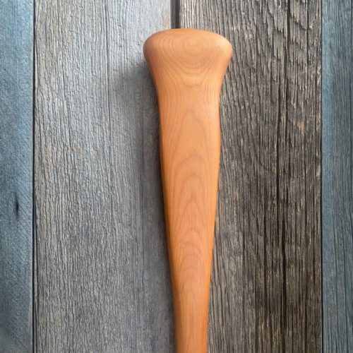 A detailed view of a cherry Woodland canoe paddle northwoods grip resting on a weathered barn board background.