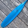 Detail of a vibrant blue tinted canoe paddle blade with a Badger paw logo, on a barn board background.