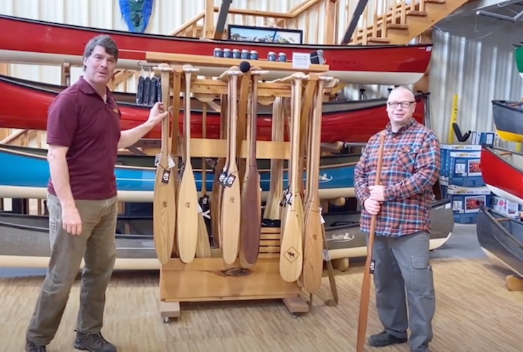 Bill Swift and Mike Ramsay stand together in front of a rack of Badger canoe Paddles and Swift canoes.